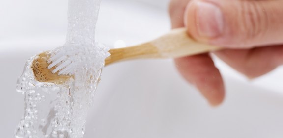 Hand spült Zahnbürste unter fließendem Wasser ab