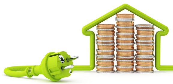 Grüner Stromstecker vor Münzstapeln in Hausform als Energiespar-Symbol