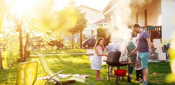 Familie grillt im sonnigen Garten vor dem Haus