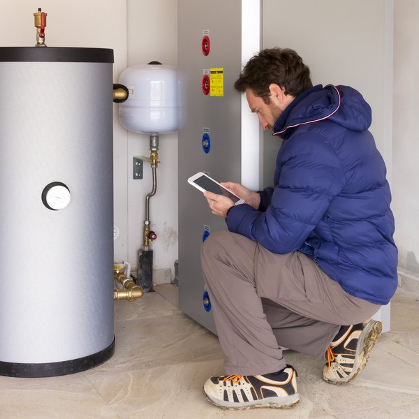 Techniker prüft mit Tablet einen großen Heizspeicher im Technikraum